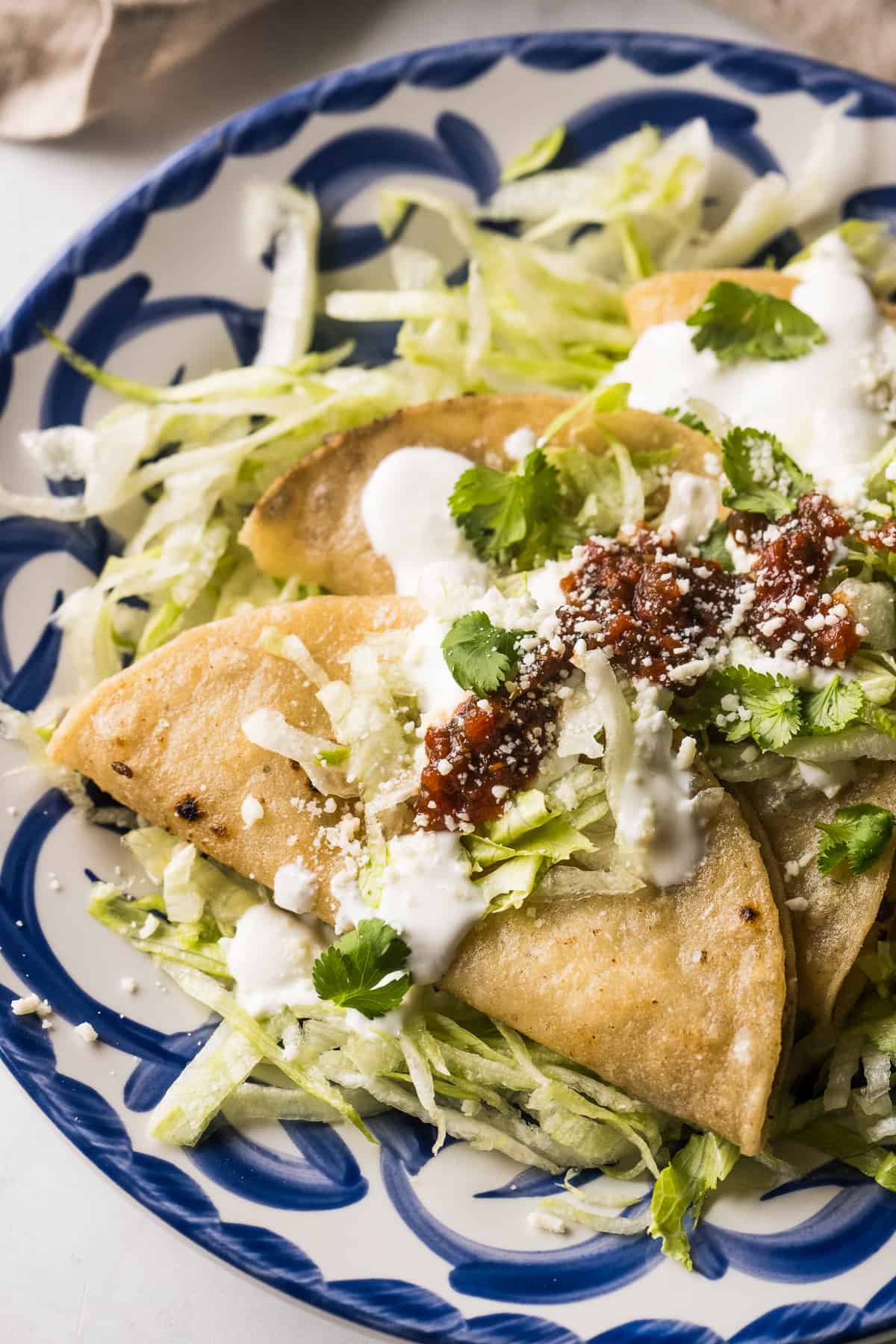 Tacos dorados on a plate served with mexican crema, red salsa, and shredded lettuce.