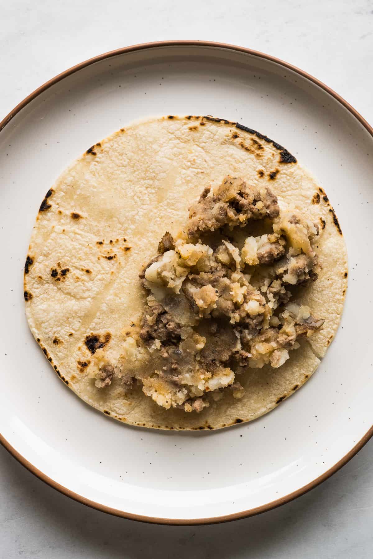 A corn tortilla with a filling of mashed potatoes and ground beef.