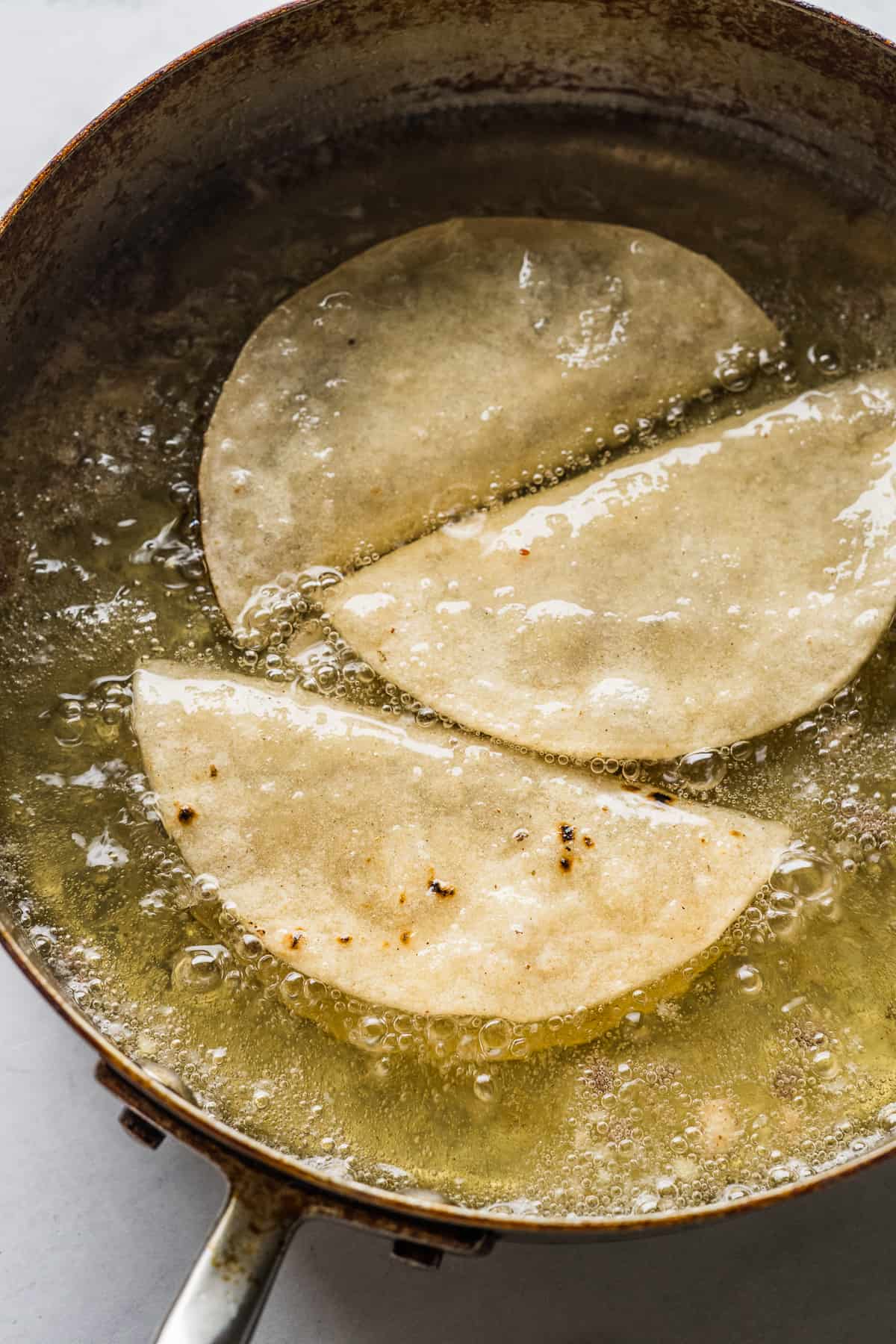 Tacos dorados frying in oil.