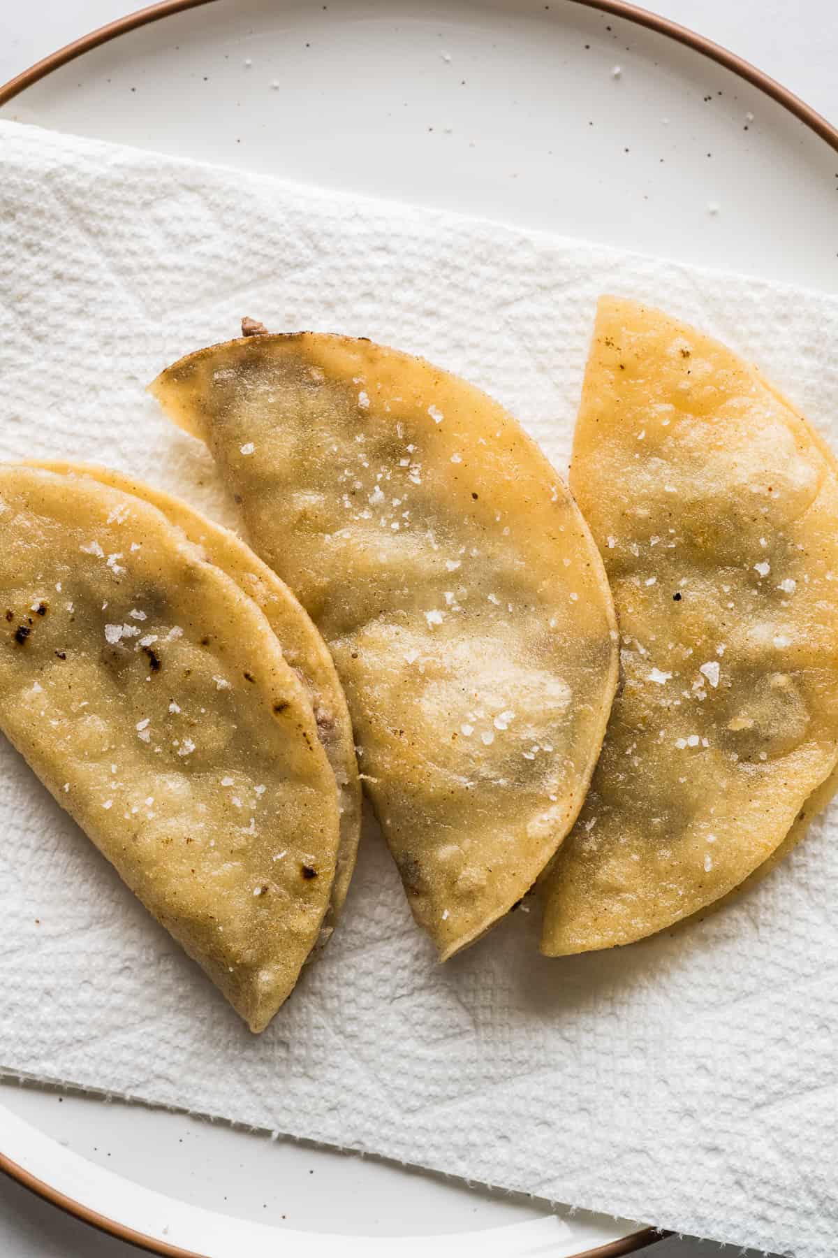 Fried tacos dorados draining on a plate with a paper towel.