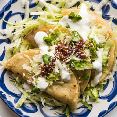 Tacos dorados on a plate served with shredded lettuce, Mexican crema, and a roasted tomato salsa.