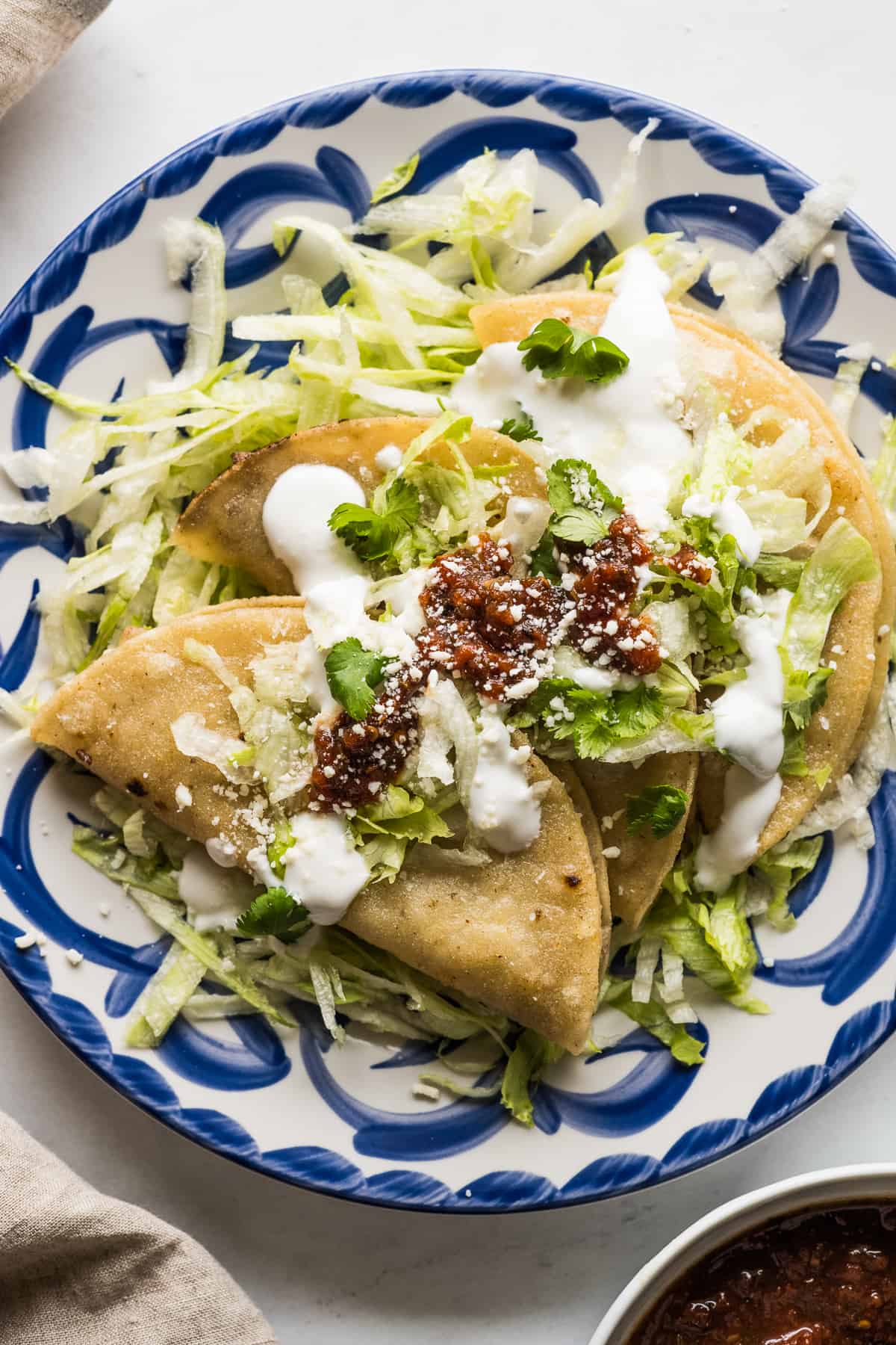 Tacos dorados on a plate served with shredded lettuce, Mexican crema, and a roasted tomato salsa.