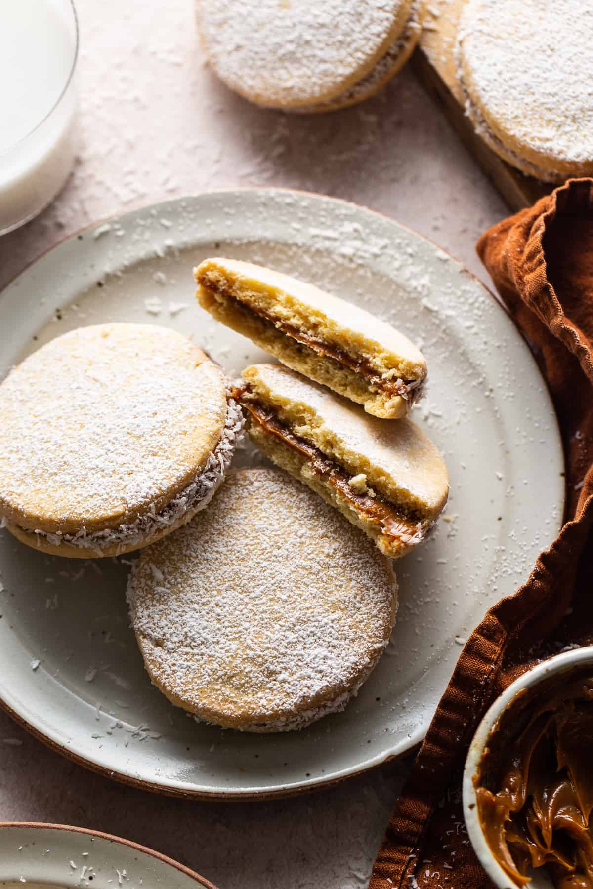3 alfajores on a plate. 1 of the alfajores is cut in half and you're able to see the gooey dulce de leche filling.
