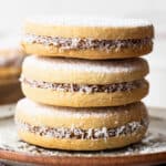 Alfajores stuffed with dulce de leche stacked on top of one another on a plate.