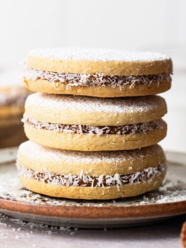 Alfajores stuffed with dulce de leche stacked on top of one another on a plate.