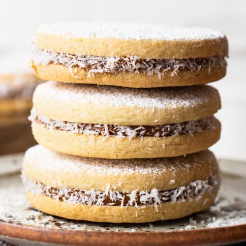 Alfajores stuffed with dulce de leche stacked on top of one another on a plate.