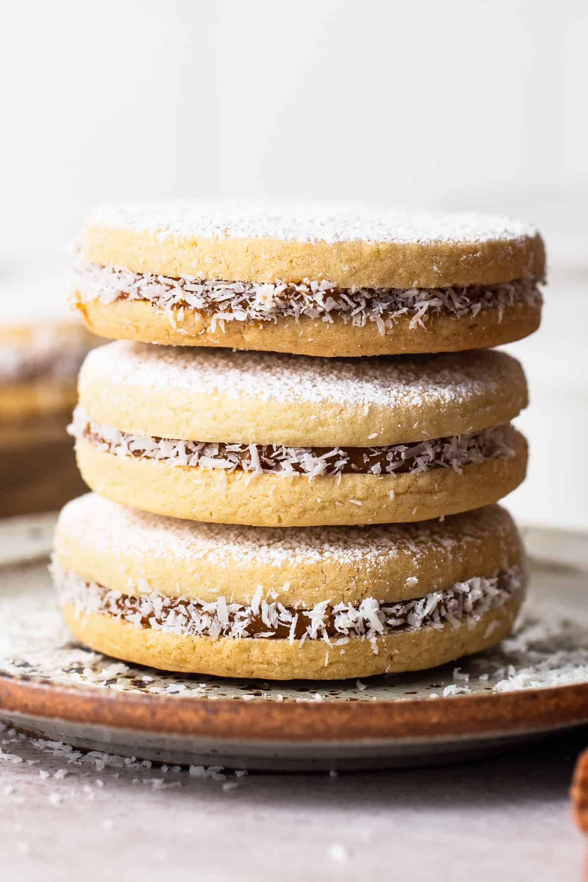 Alfajores stuffed with dulce de leche stacked on top of one another on a plate.