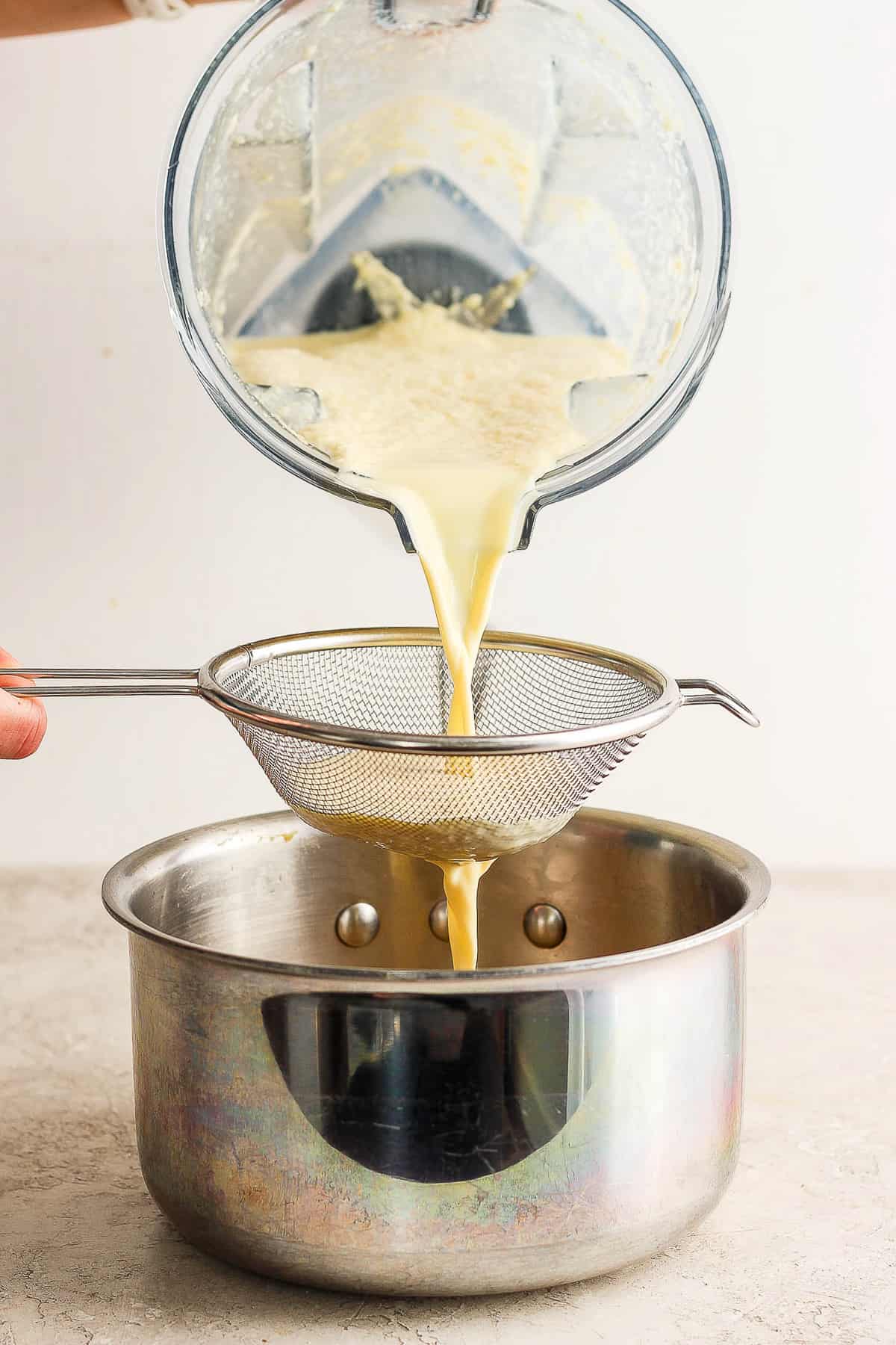 The blended corn mixture being poured through a fine mesh strainer and into a pot.