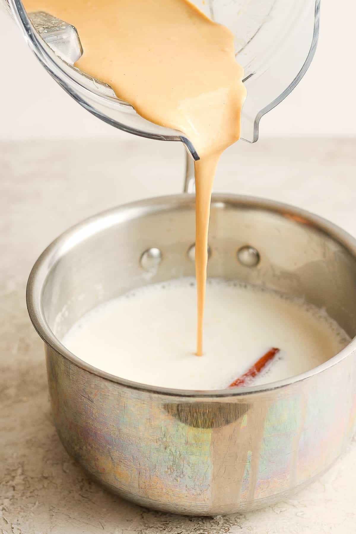 Blended marias cookies mixture being poured into a saucepan of hot milk.