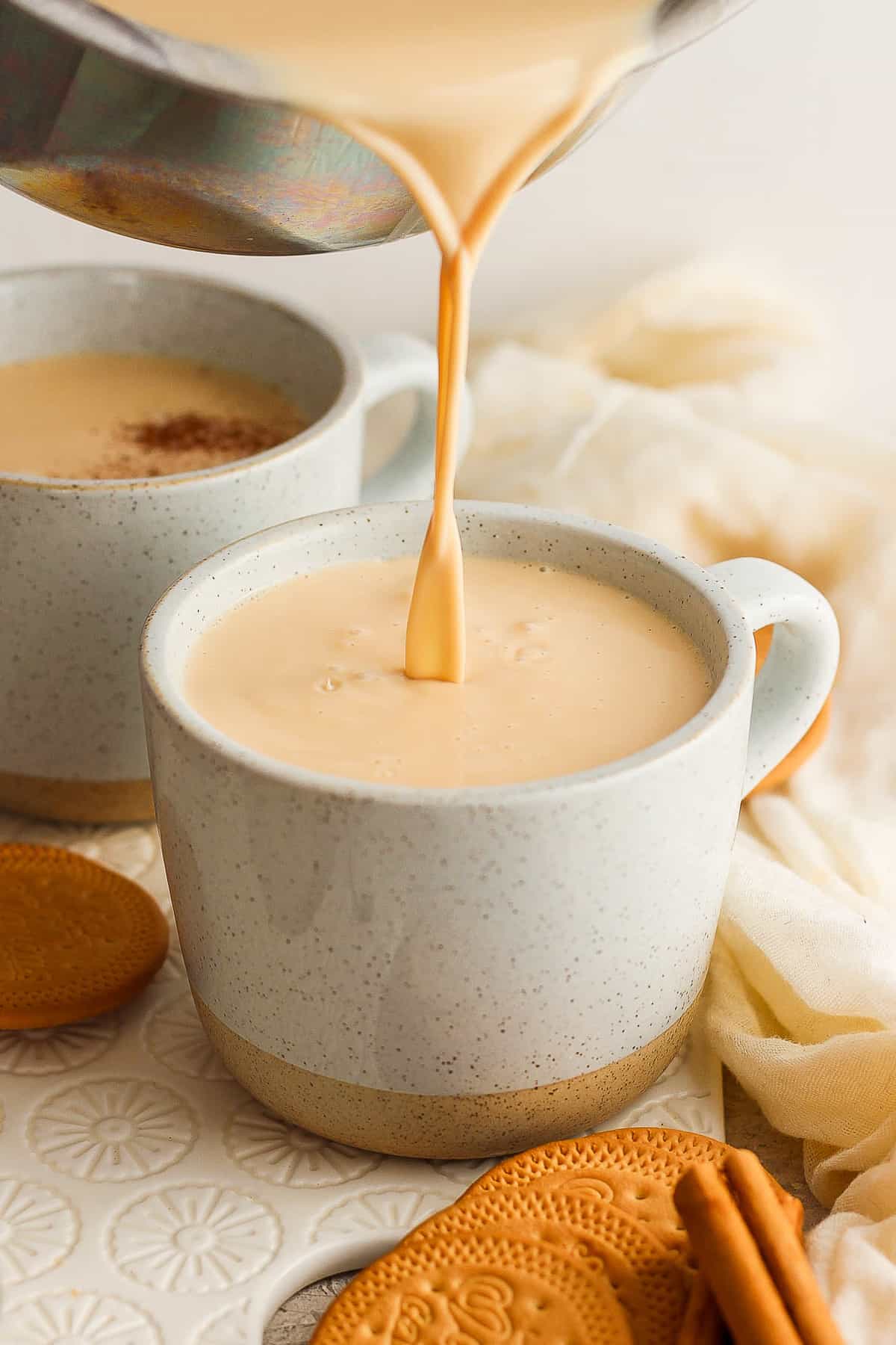 Warm atole de galletas being poured into a mug and topped with ground cinnamon