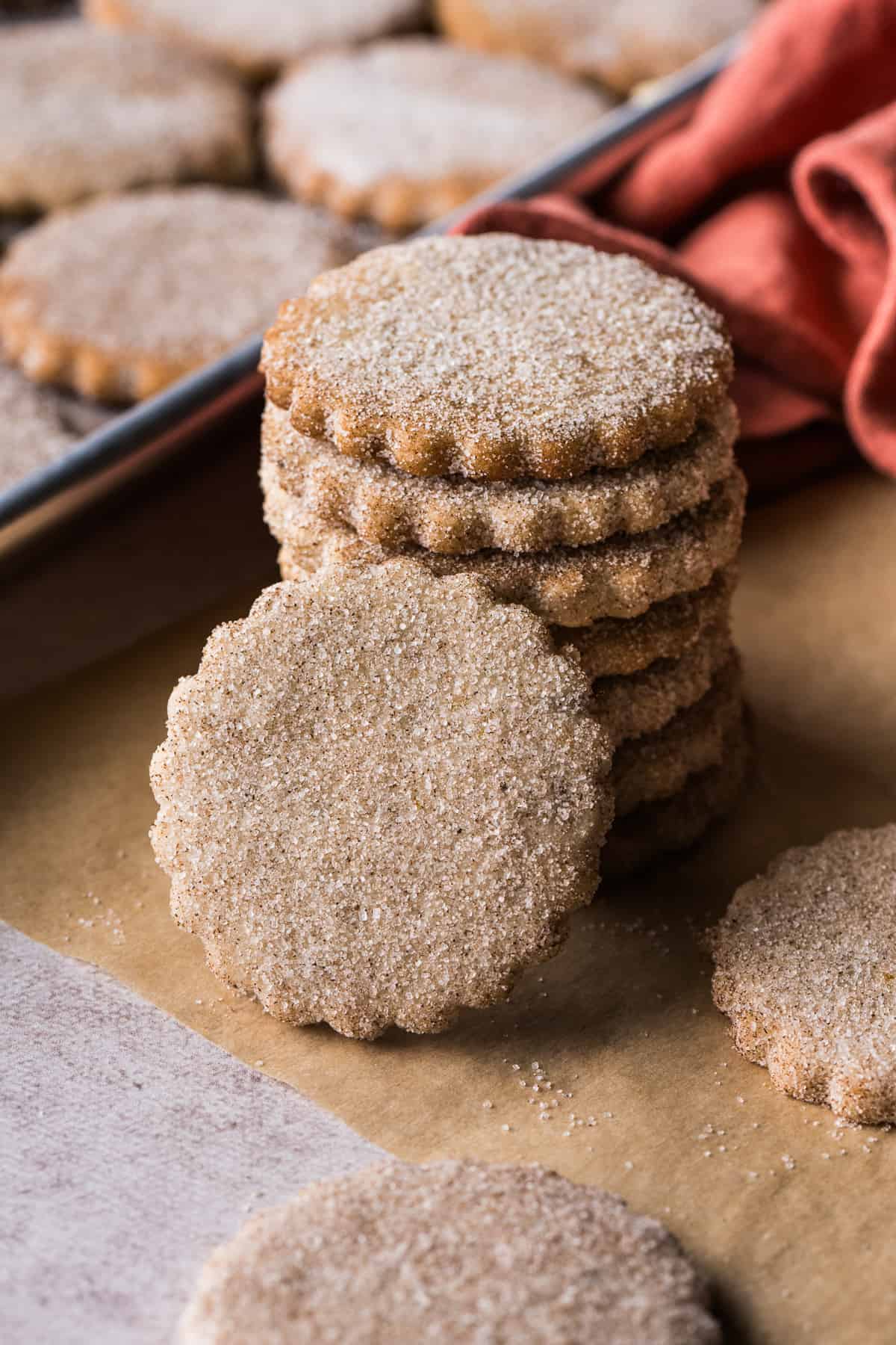 Biscochitos covered in cinnamon sugar stacked on top of one another on a piece of parchment paper.