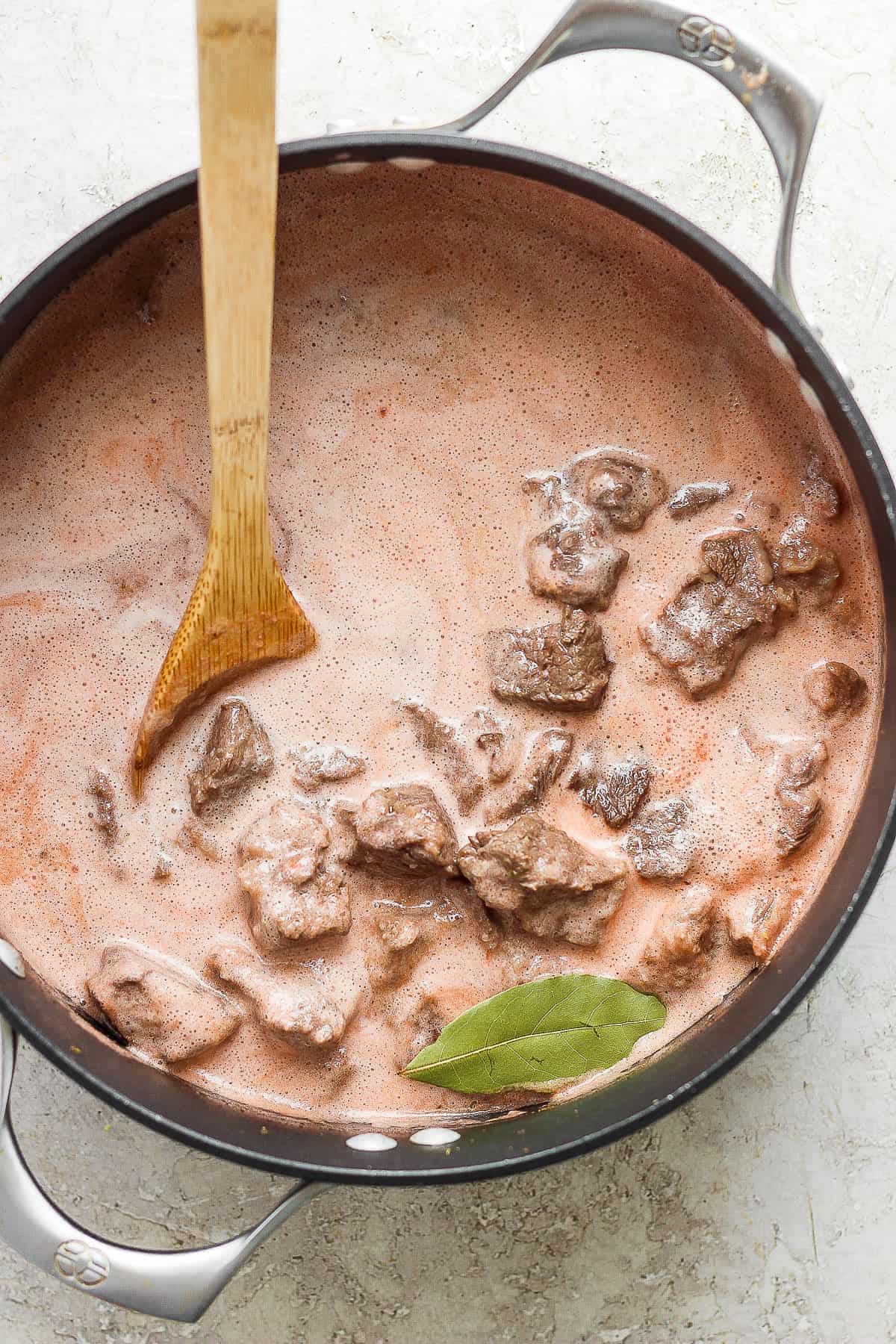 Tomato broth in a pot with chunks of beef chuck roast.