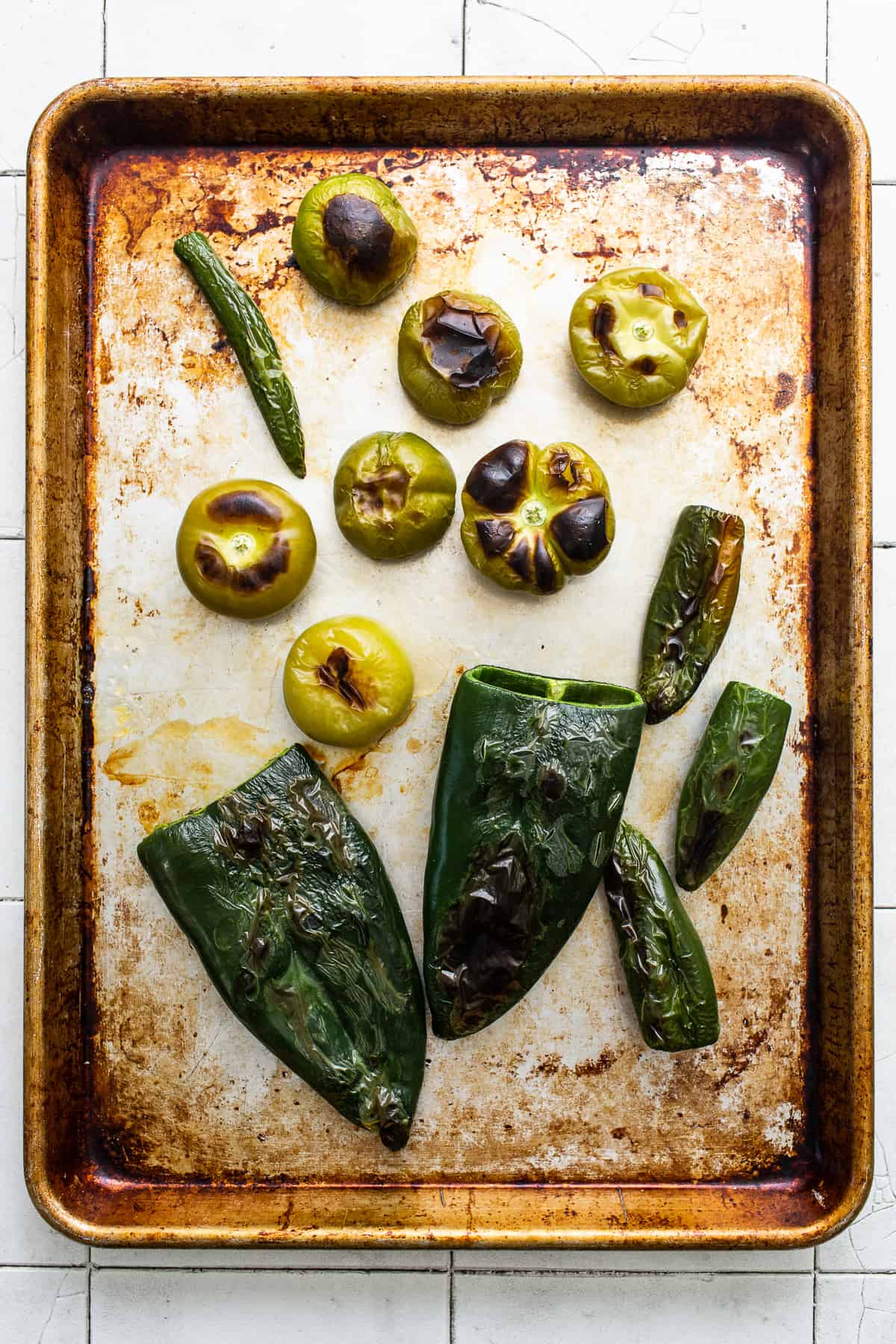 Roasted tomatillos, jalapeños, and poblanos on a baking sheet.