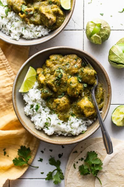 Chile verde in a bowl served on top of some cilantro lime rice, fresh cilantro, and lime wedges.