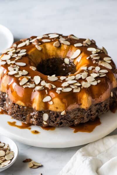 Chocoflan topped with cajeta and sliced almonds on a cake stand.