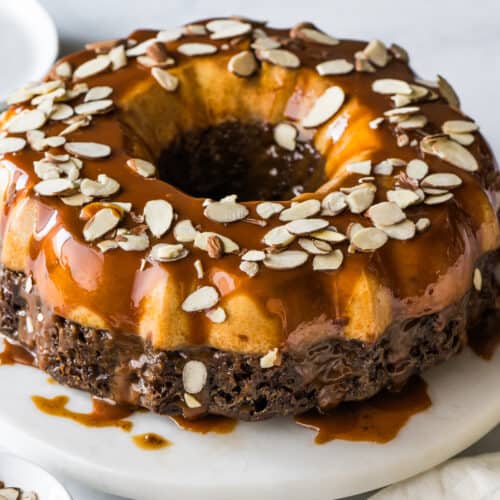 Chocoflan topped with cajeta and sliced almonds on a cake stand.