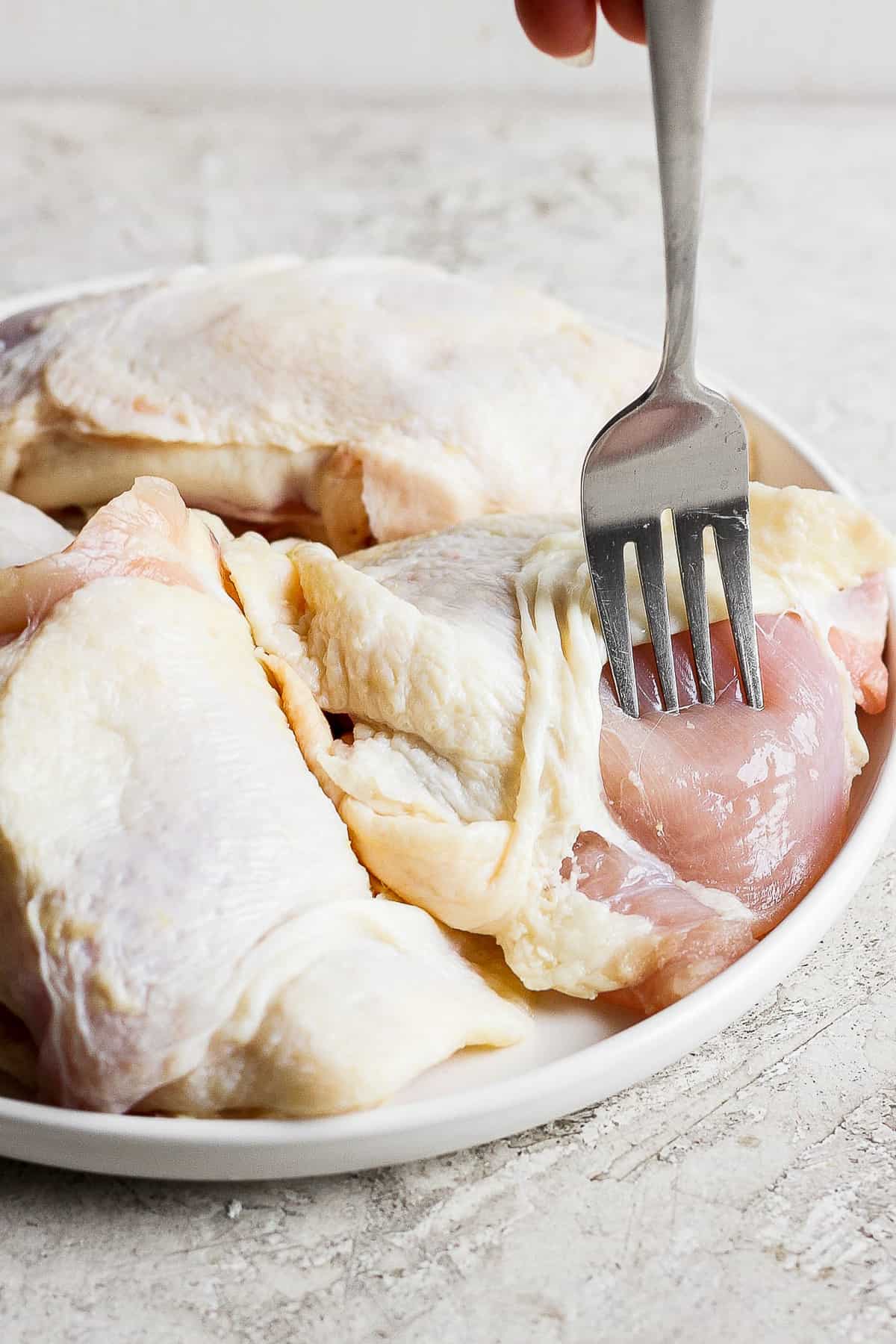Chicken thighs being pricked with a fork.
