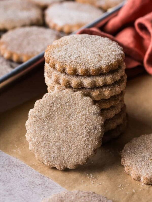 Biscochitos covered in cinnamon sugar stacked on top of one another on a piece of parchment paper.