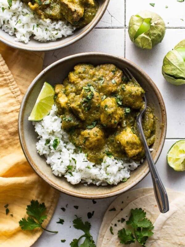 Chile verde in a bowl served on top of some cilantro lime rice, fresh cilantro, and lime wedges.