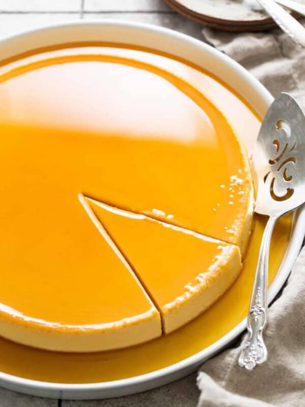 Flan de queso with caramel on top on a serving plate with a slice cut out ready to be served.