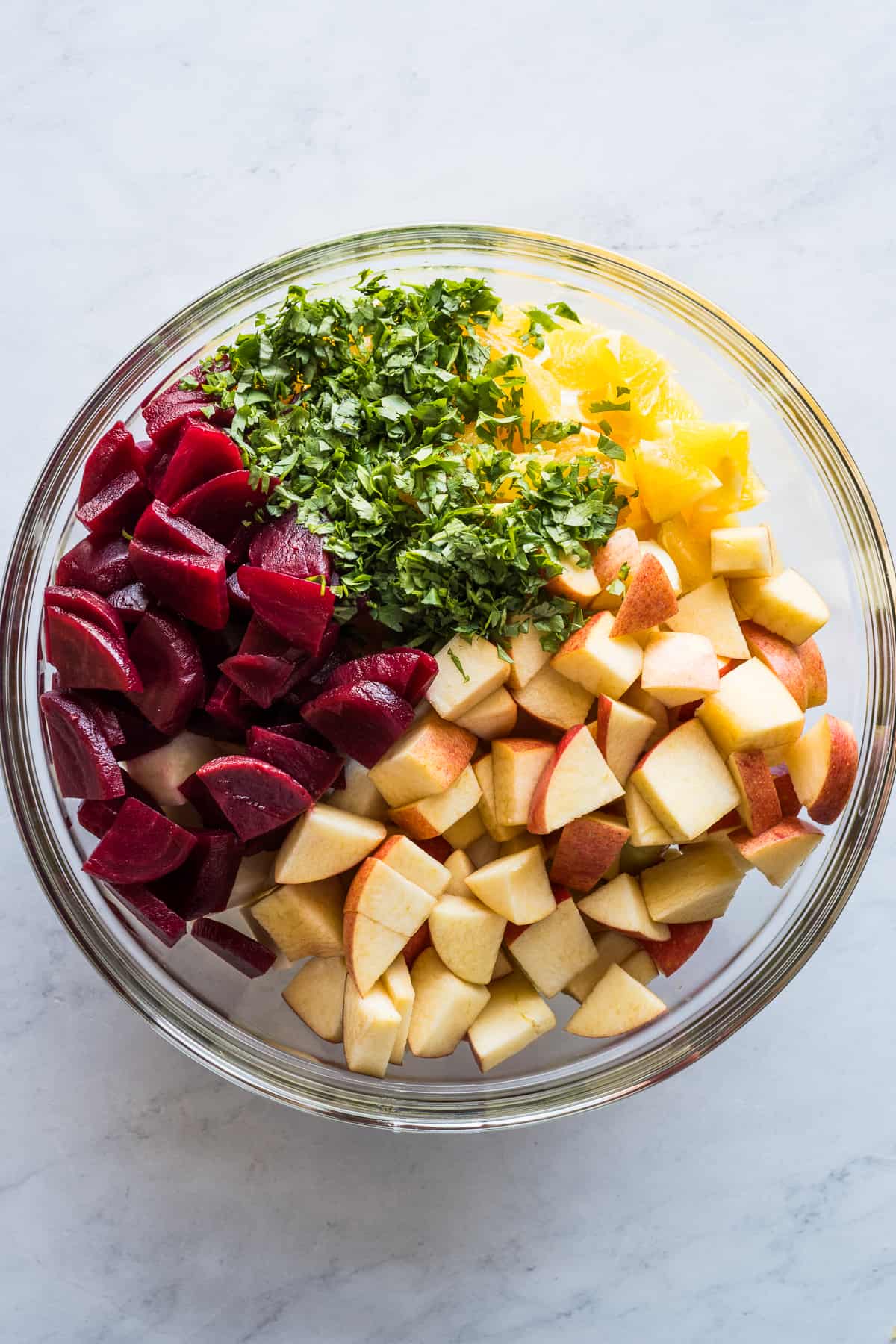 Beets, apples, oranges, jicama, cilantro, and more in a large bowl.