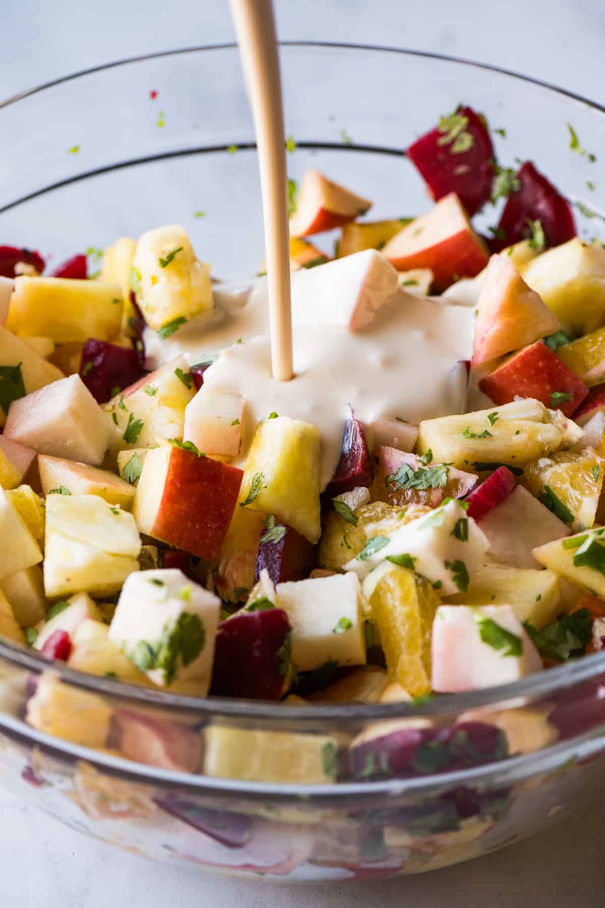 The sweet and creamy dressing for ensalada de nochebuena being poured in a bowl of fruit.