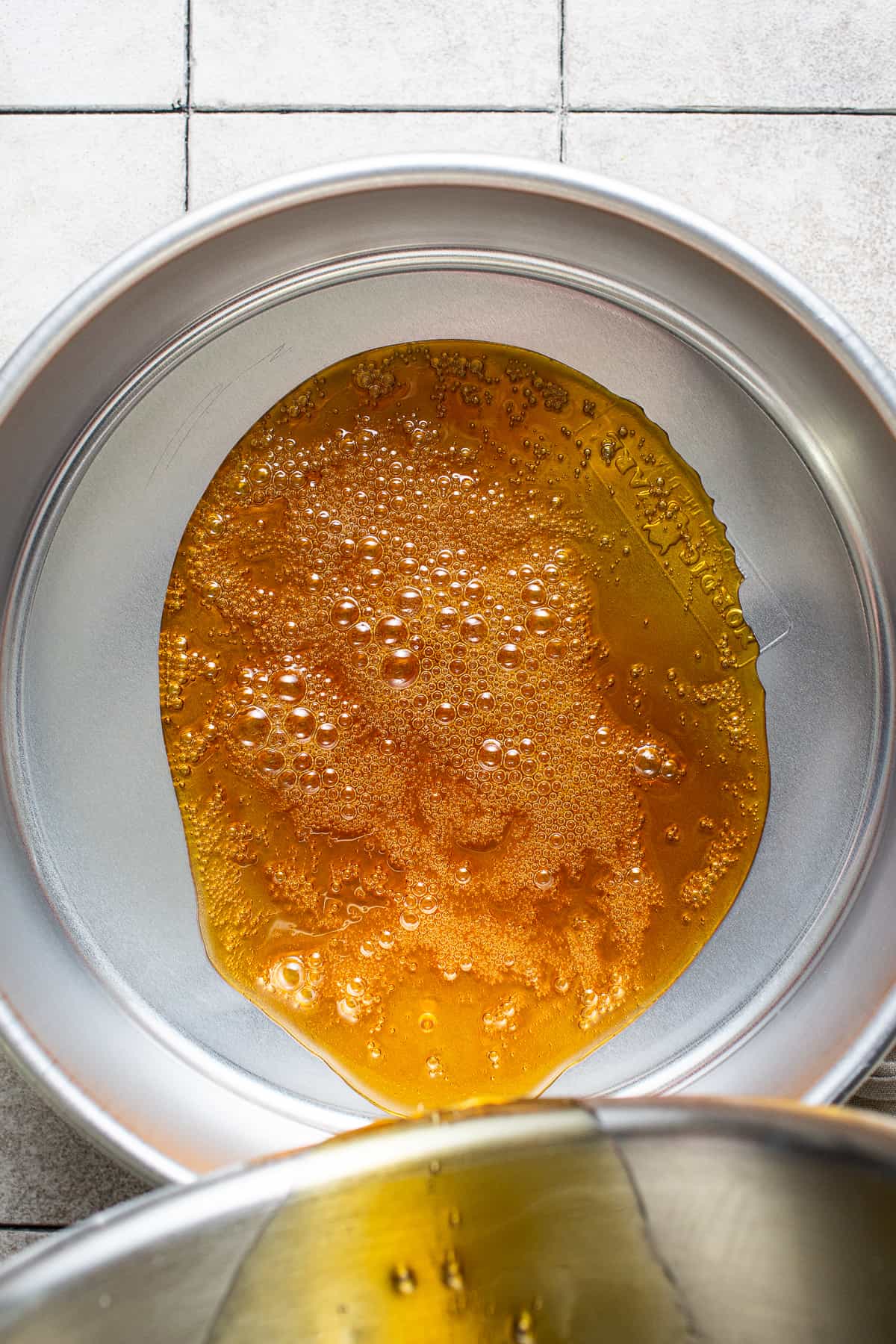 Caramel being poured into a round cake pan for flan de queso.