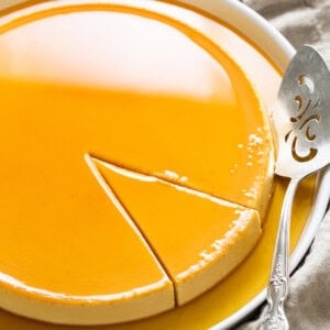 Flan de queso with caramel on top on a serving plate with a slice cut out ready to be served.