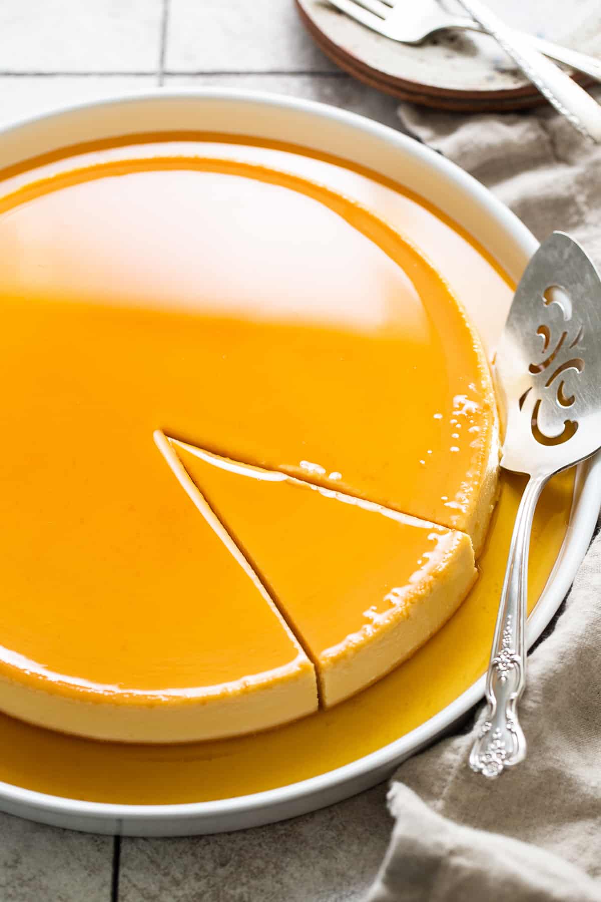 Flan de queso with caramel on top on a serving plate with a slice cut out ready to be served.