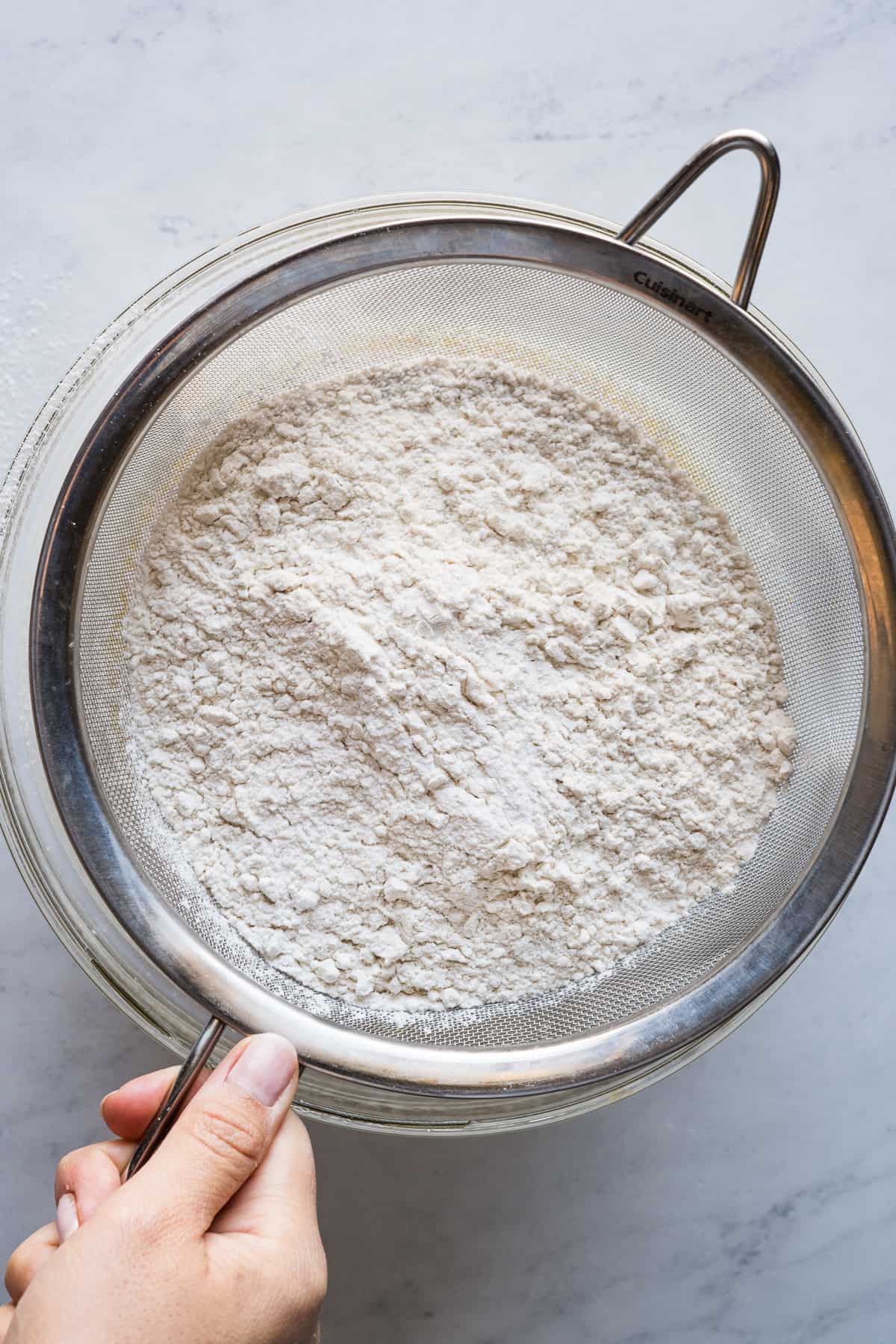 Flour being sifted through a fine mesh strainer into a bowl.