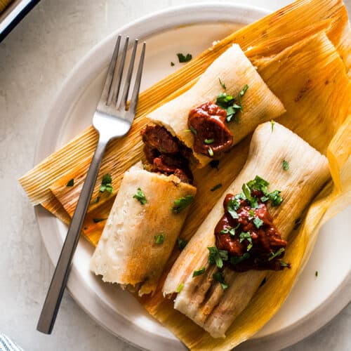 Learn how to make tamales right at home with these simple step-by-step instructions! This authentic Mexican tamales recipe is filled with tender pieces of pork simmered in a delicious red chile sauce wrapped in a soft and fluffy masa dough.