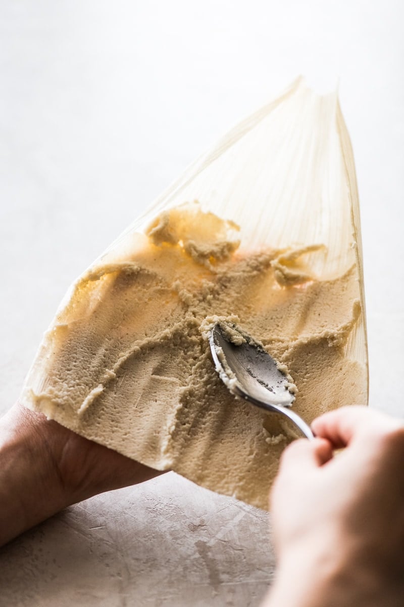 Fresh masa dough being spread on a corn husk for tamales.