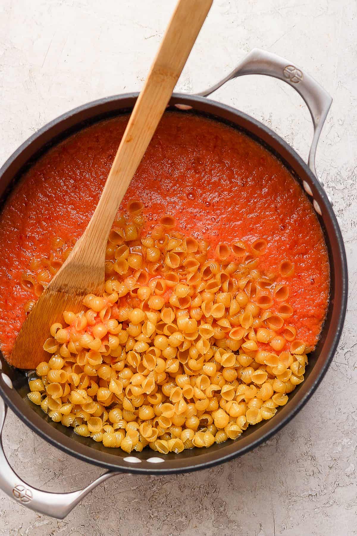 Blended tomato broth being stirred into a pot of toasted shell pasta to make some sopita de conchas.