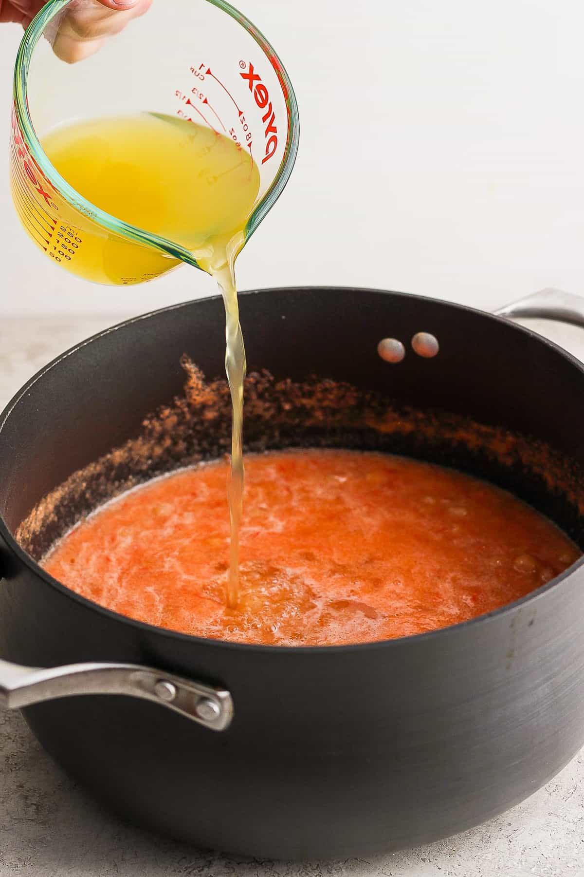 Vegetable broth being poured into a pot of sopa de conchas.