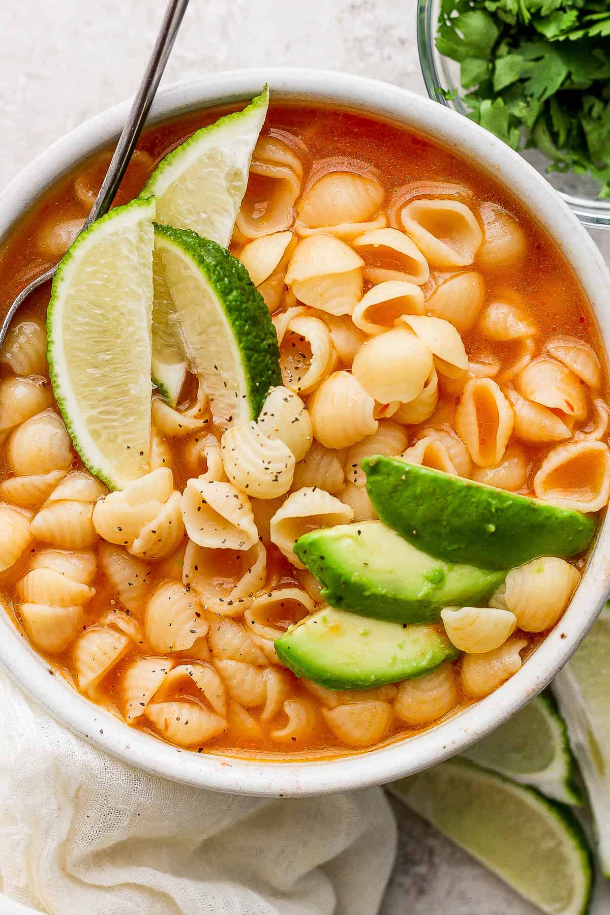 Sopa de conchas in a white bowl topped with sliced avocado.