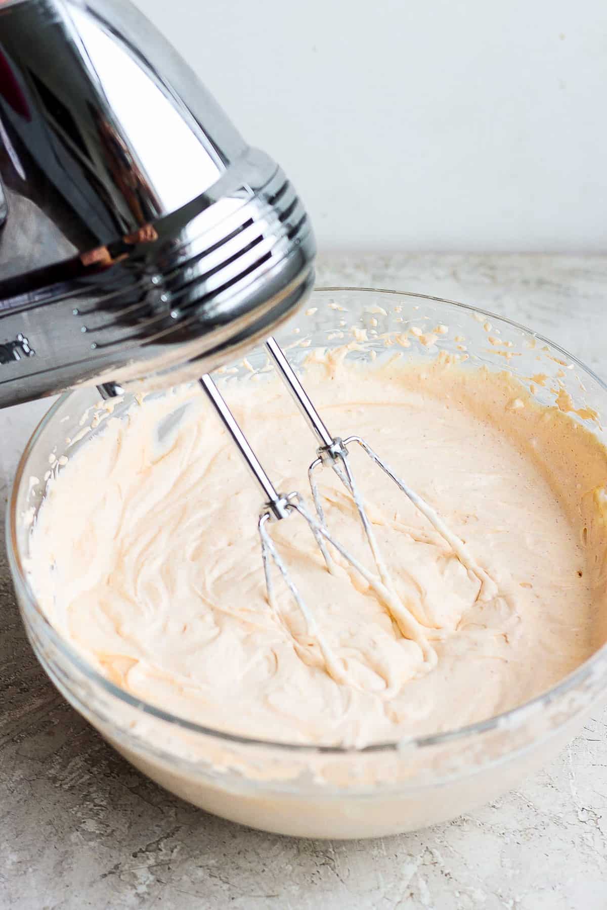 The base layer of taco dip being mixed with an electric mixer.