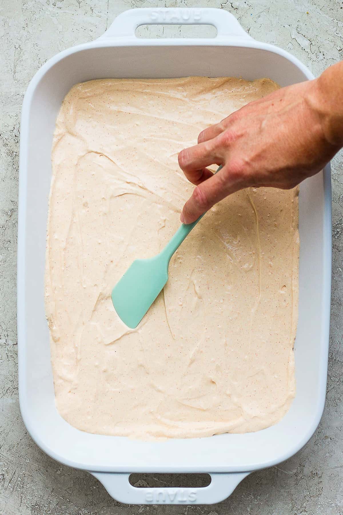 The cream cheese and sour cream mixture of taco dip being spread in a large baking dish.