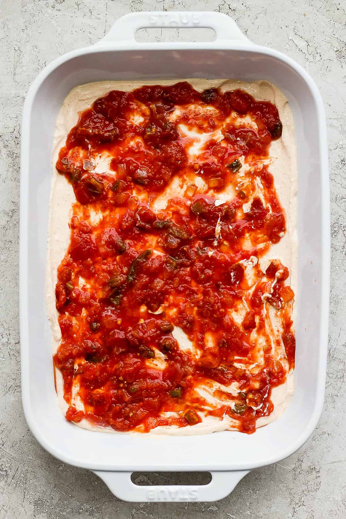 Chunky salsa in a baking dish layered on top of cream cheese.