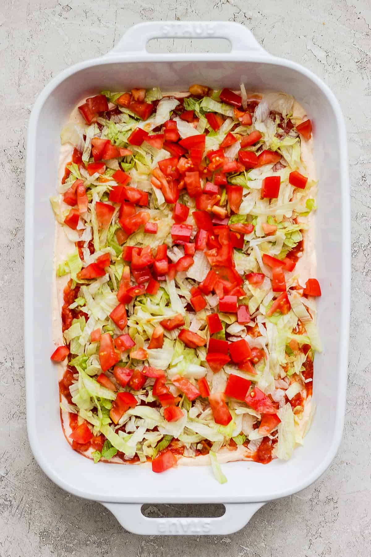 Lettuce and tomatoes in a baking dish of taco dip.