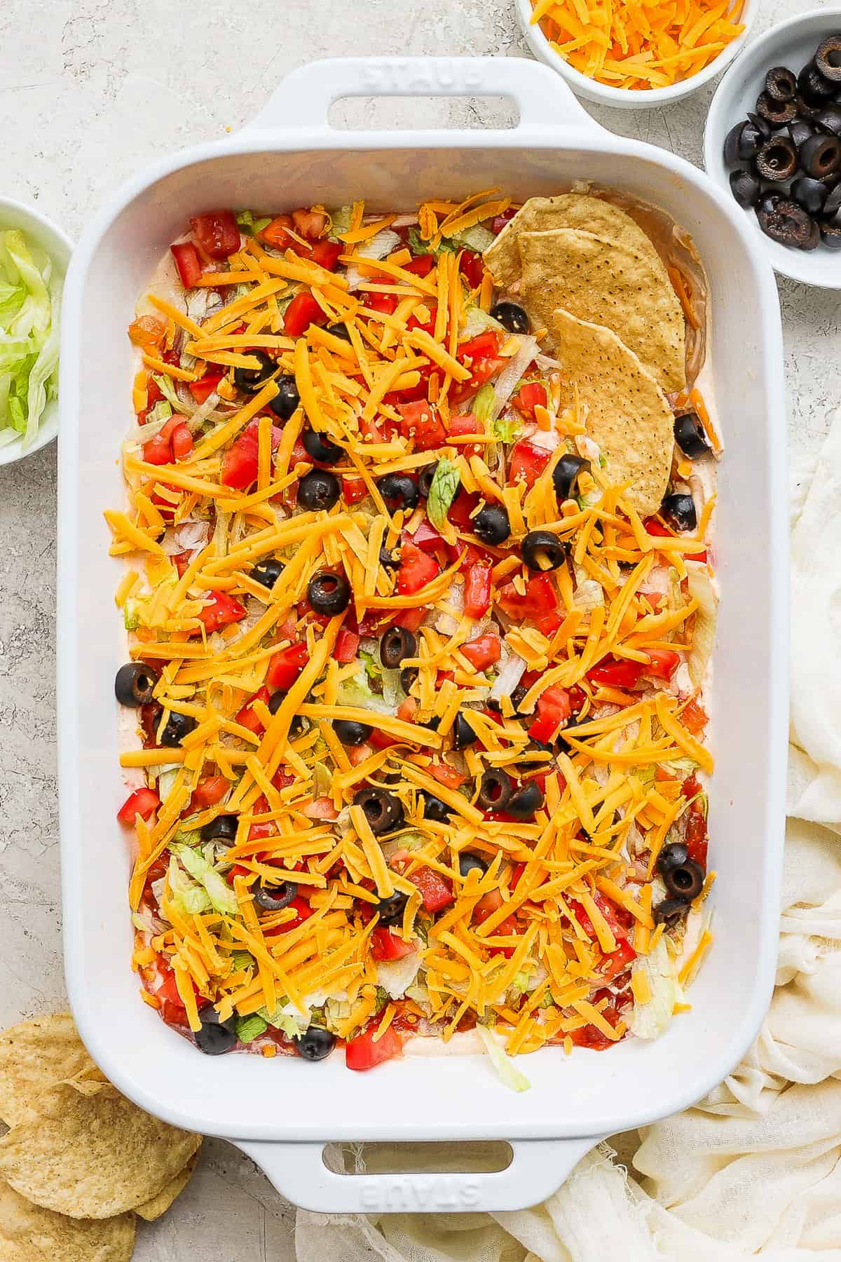 Taco dip in a baking dish topped with shredded cheese, tomatoes, and olive served with tortilla chips.