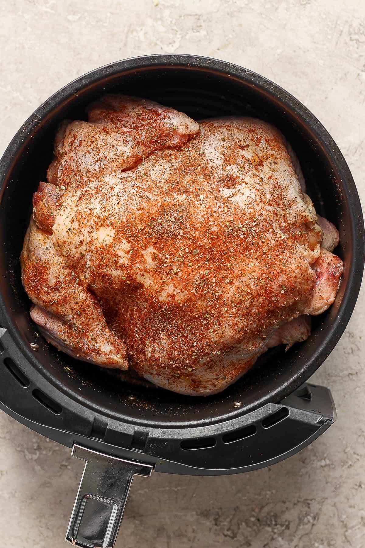 A seasoned chicken in the basket of an air fryer before being cooked.