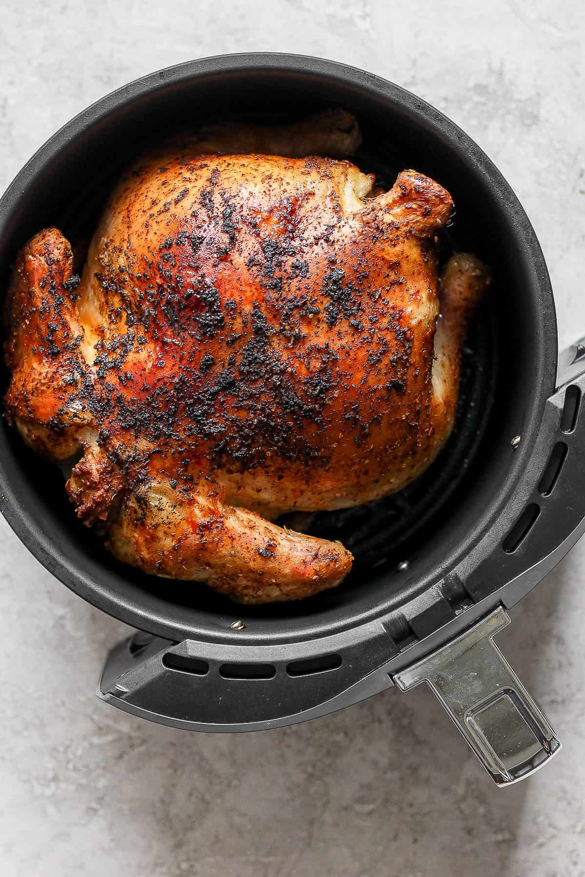 A whole chicken in an air fryer cooked on one side before being flipped.