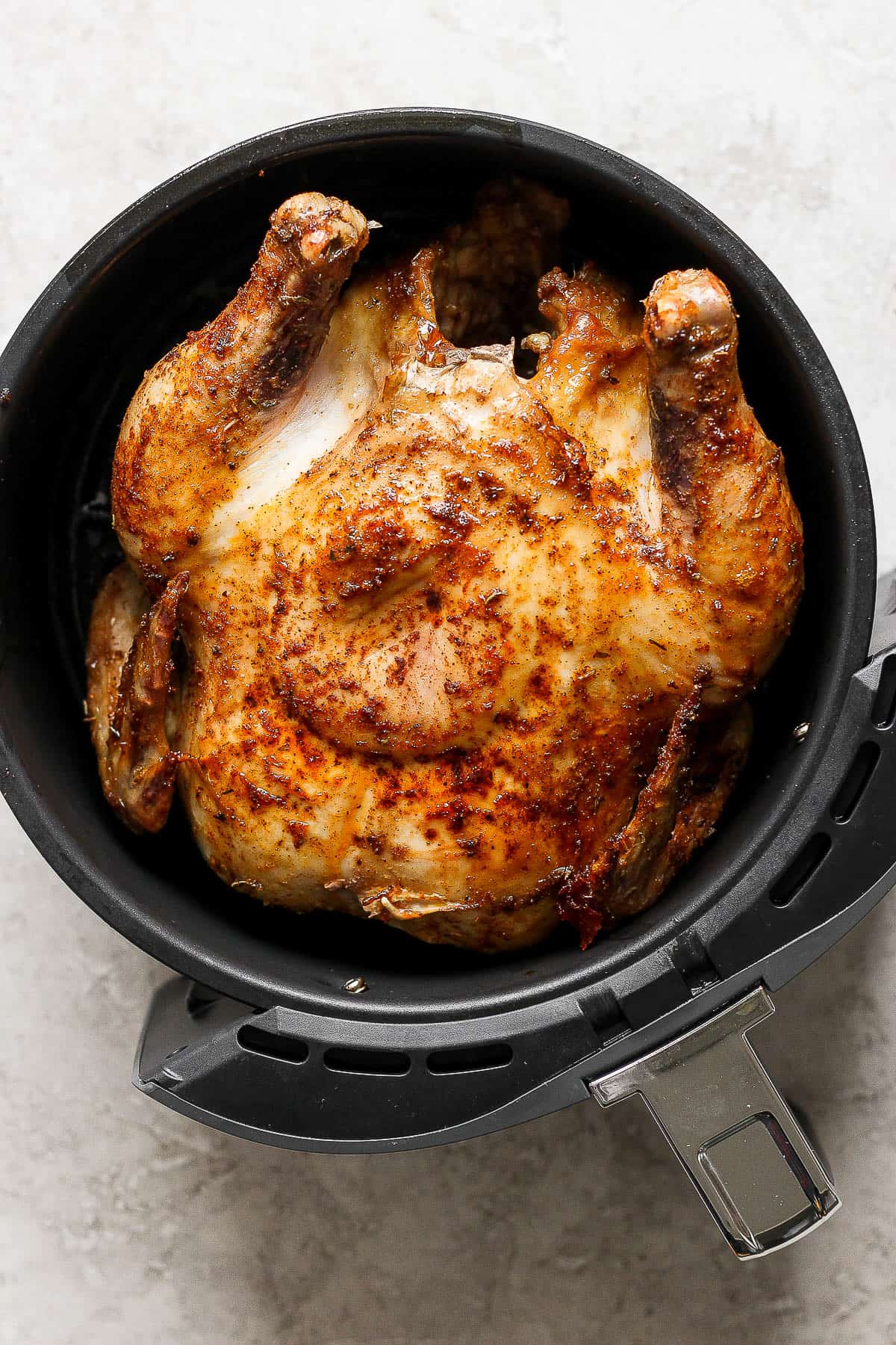 A whole chicken in an air fryer with the breast side up.