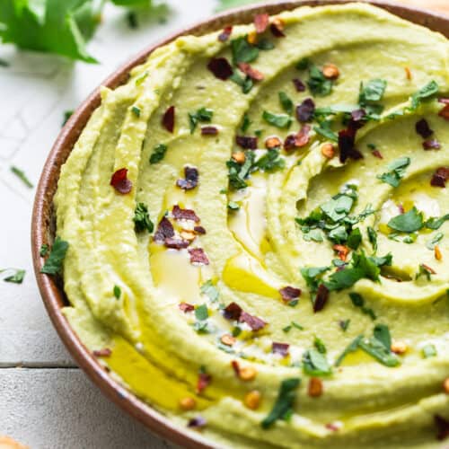 Avocado hummus garnished with a drizzle of olive oil, chopped cilantro, and red pepper flakes.
