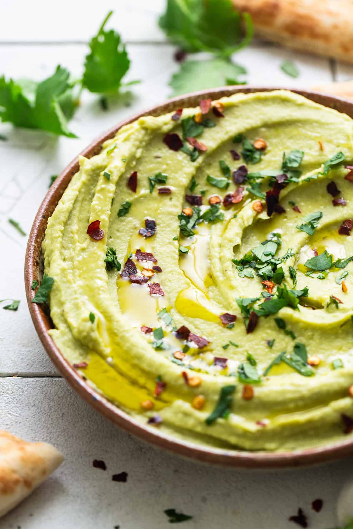 Avocado hummus garnished with a drizzle of olive oil, chopped cilantro, and red pepper flakes.