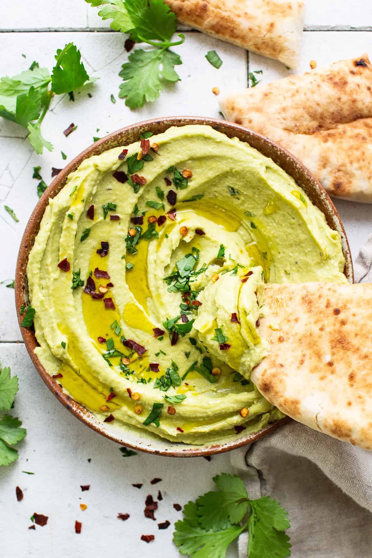 A slice of pita bread being dipped in a bowl of avocado hummus.