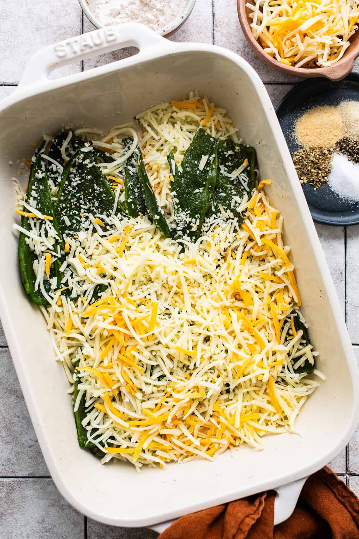 Roasted poblano peppers in a baking dish with shredded cheese.