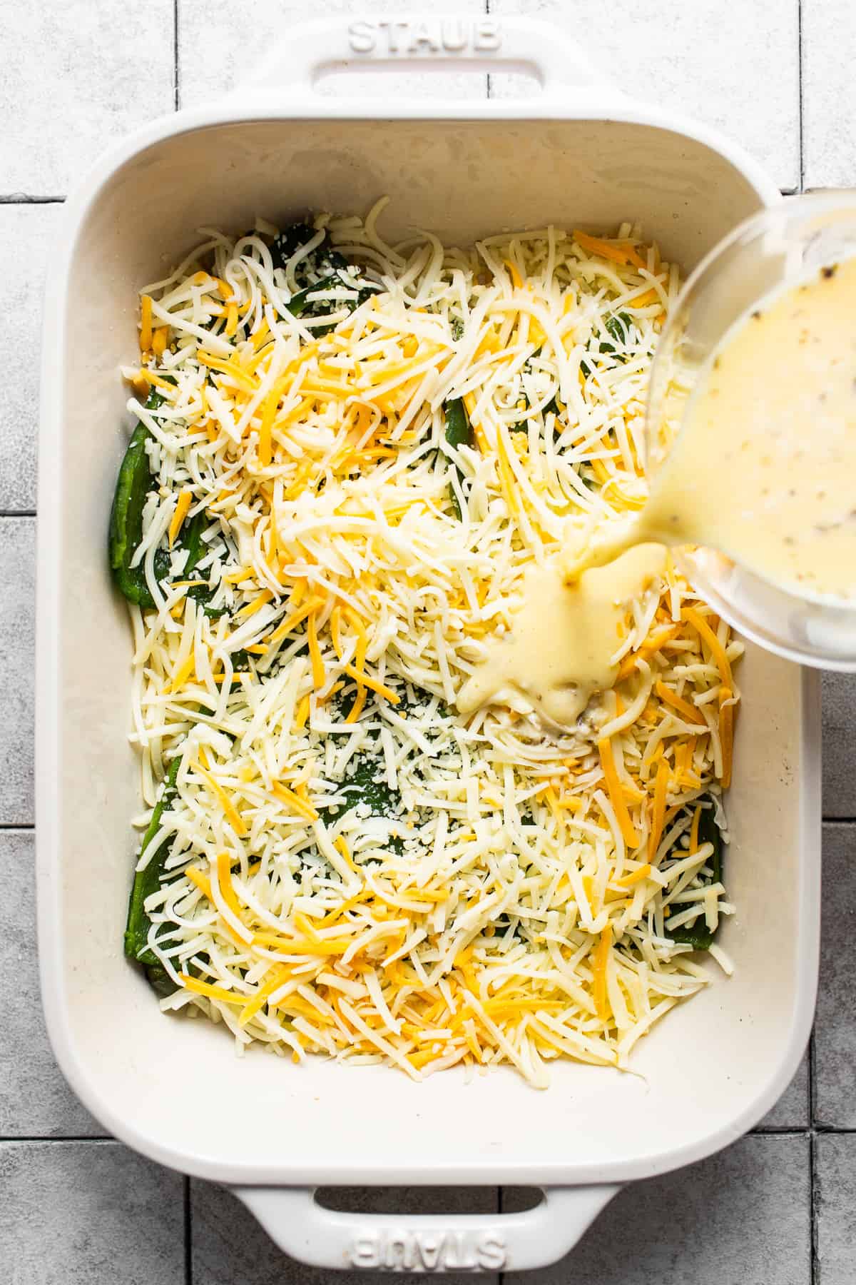 The egg mixture for chile relleno casserole being poured into a large baking dish.