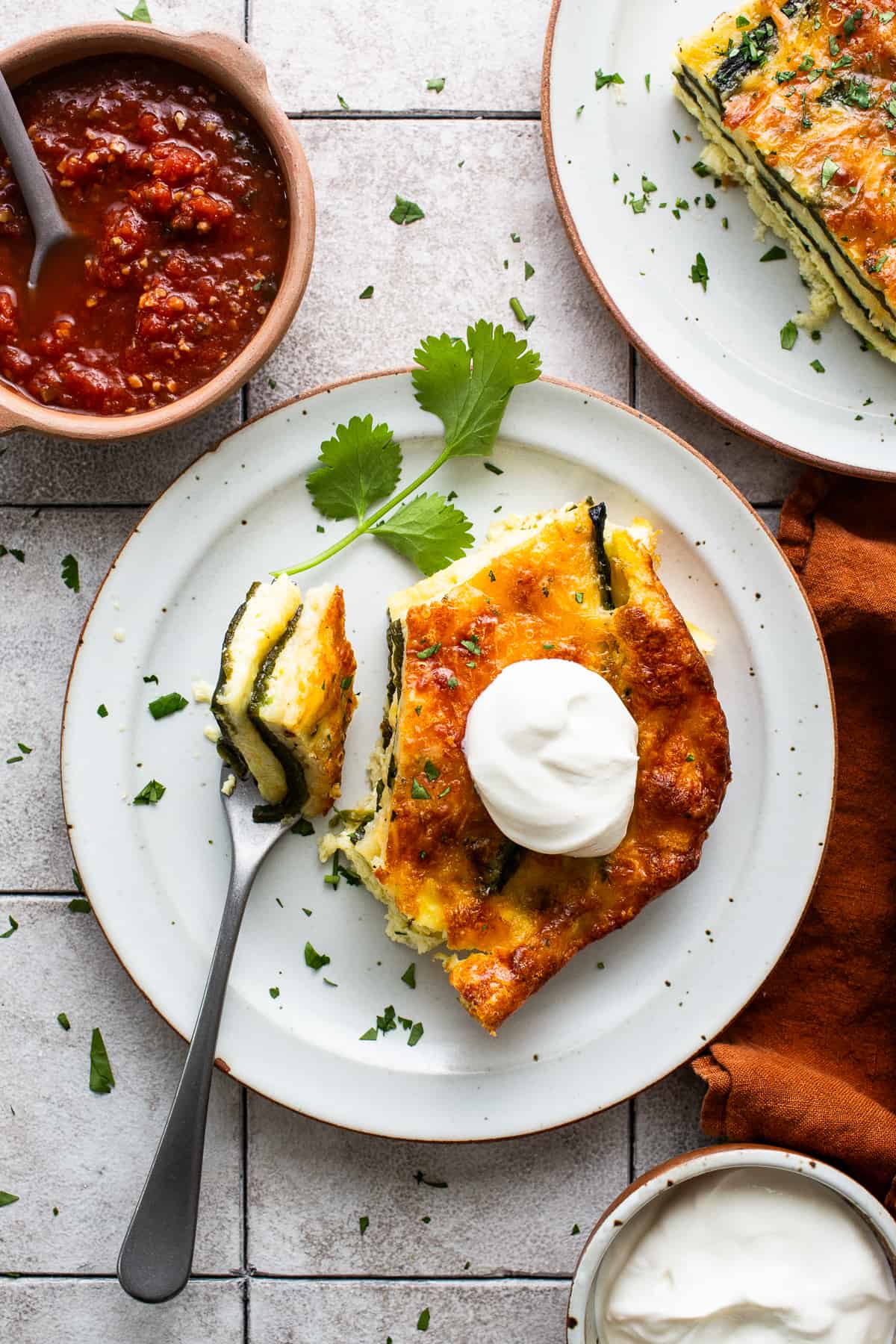 A slice of chile relleno casserole on a plate served on a dollop of sour cream.