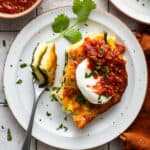 A slice of chile relleno casserole served with sour cream and salsa.